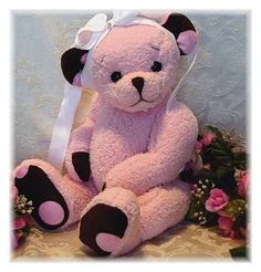 a pink teddy bear sitting on top of a table next to some flowers and greenery