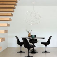 a dining table with four chairs and a vase on it in front of some stairs