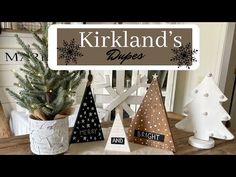 three small christmas trees sitting on top of a wooden table next to a sign that says kirkland's pines