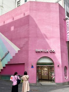 two women are standing in front of a pink building that says banila co on it