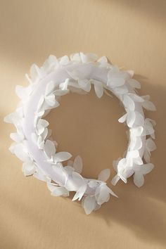 a white wreath made out of paper flowers on top of a brown surface with shadow