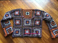 a colorful crocheted sweater is laying on the floor next to a wooden floor