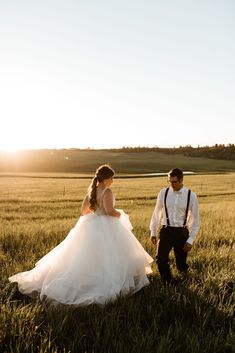 a bride and groom standing in a field at sunset