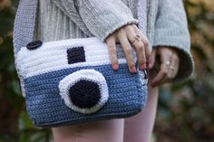 a woman holding a blue and white crocheted bag with a camera on it