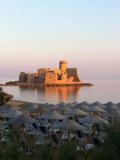 the beach is lined with umbrellas and chairs near an old castle in the distance