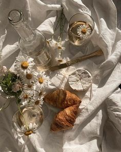 an assortment of food and drinks on a white cloth with flowers in glass vases