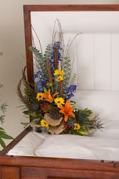 an arrangement of flowers in a wooden box on a bed with white sheets and pillows