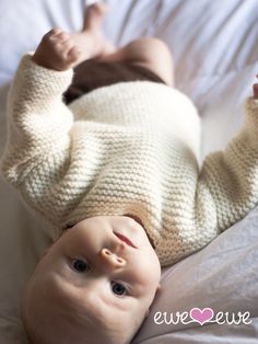 a baby laying on top of a bed wearing a white knitted sweater and pants