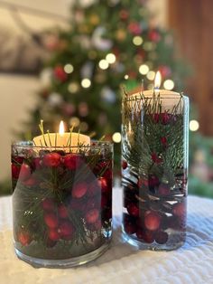 two glass vases filled with berries and greenery next to a lit christmas tree