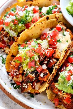 three tacos on a plate with guacamole and salsa