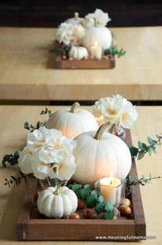 two wooden trays with white pumpkins, flowers and candles in them on a table