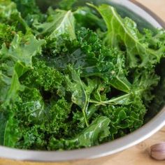 a bowl filled with green vegetables on top of a wooden table