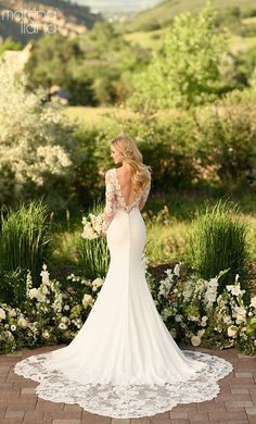 a woman in a white wedding dress standing on a brick walkway with flowers and greenery behind her