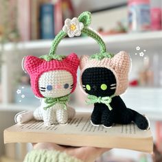 two small crocheted cats sitting on top of a book