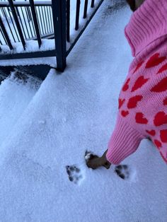 a person standing in the snow with their foot prints on it's ground and wearing a pink sweater