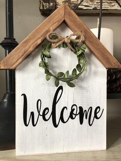 a welcome sign hanging from the side of a wooden house with a wreath on top