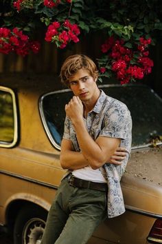 a young man leaning against a car with flowers hanging from the roof and his hand on his chin