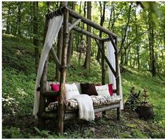 a bed made out of branches in the woods with pillows and blankets on it's sides