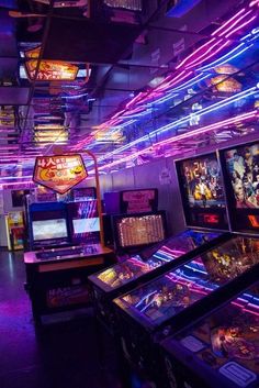 several pinball machines are lined up in a room with neon lights on the ceiling