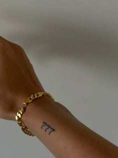 a person's arm with a gold chain bracelet and the word pi tattooed on it