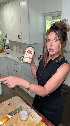 a woman holding a jar of food in her hand and pointing to it on the counter