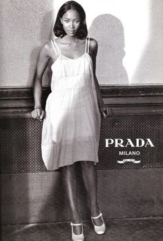 a black and white photo of a woman standing in front of a prada sign