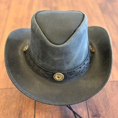 This hat is crafted from Crazy Horse Leather and features a braided band with conchos.  It includes a sweatband on the inside for comfort. Made with handcrafted leather for both men and women.  Its available in both tan and black natural leather colors.  It is unlined on the inside.  The wide brim of this leather hat provides shade in the sun.  You can make your own style as the brim of the hat is easily shapable. It is made from 100% pure leather. The hat is approximately 3" brim and 3 ½'' Crown in size. It has a distressed finish on all the leather.  It includes a chinstrap which is removable and adjustable to the customer's preference.  Please refer to the size chart as shown in the pictures to select the perfect size for you and to place an order with confidence. Rugged Leather Hat With Flat Brim, Rugged Leather Fedora Hat, Black Rustic Adjustable Hat, Adjustable Leather Fedora, Rugged Adjustable Leather Hat, Rugged Adjustable Fedora Hat, Adjustable Rugged Fedora Hat, Adjustable Rugged Leather Hat, Adjustable Rugged Leather Hat Bands