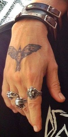 a close up of a person's hand with two rings on it and a bird tattoo