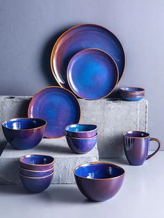 blue dishes and cups are stacked on top of each other in front of a gray wall