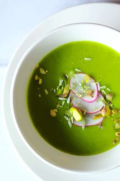 a white bowl filled with green soup topped with radishes and pistachio