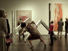 a group of people looking at paintings in an art gallery with one woman holding a cross