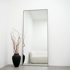 a black vase sitting in front of a mirror on the floor next to a white couch