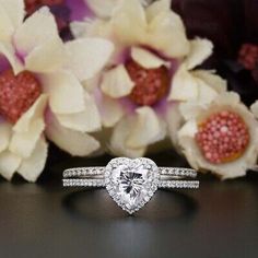 a heart shaped diamond ring sitting on top of a table next to some white flowers