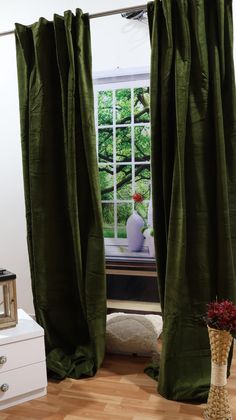 a vase with flowers in it sitting next to two green drapes on a window sill