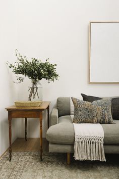 a living room with a couch, coffee table and plant on the side tables in front of it