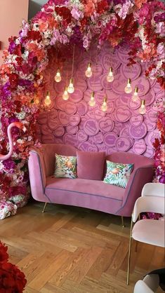 a pink couch sitting under a purple wall with flowers on it and lights hanging from the ceiling