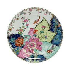 a plate with flowers and birds painted on the front, sitting on a white surface