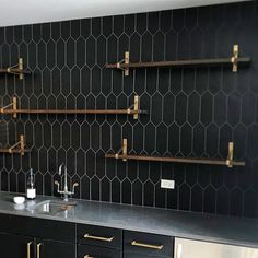 a kitchen with black tiles and gold accents on the wall, along with brass handles