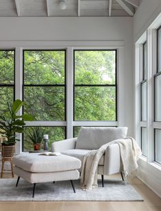 a living room with large windows and a white couch next to a plant on the floor