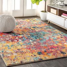 a brightly colored rug in a living room with a plant on the floor and a white chair