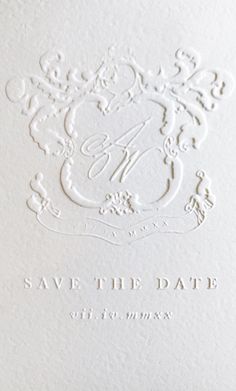 an ornate monogrammed save the date card is shown in white paper with black ink