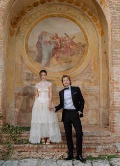 two people standing next to each other in front of a wall with paintings on it