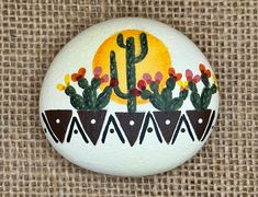 a painted rock with cactuses and flowers in the pot on burlocked fabric