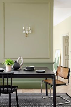 a dining room table with two chairs and a tea pot on it, in front of a green paneled wall