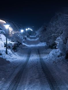 a snowy street at night with snow on the ground and lights in the dark above