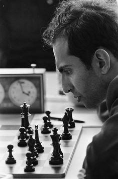 a man sitting at a chess board with his hand on the queen's pawn