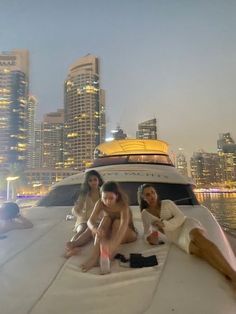 three women sitting on the back of a boat in front of a cityscape