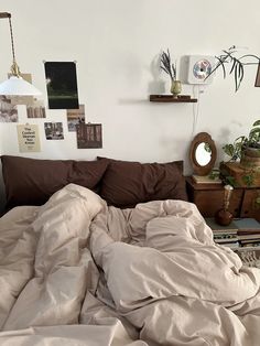 an unmade bed in a bedroom with many pictures on the wall and plants hanging above it