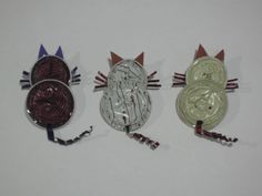 three cat shaped magnets are shown on a white surface, one is silver and the other is red