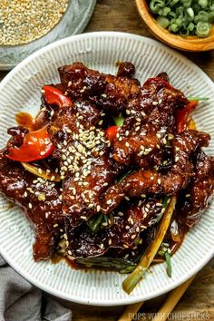 a white plate topped with beef and vegetables covered in sesame seeds next to bowls of green beans